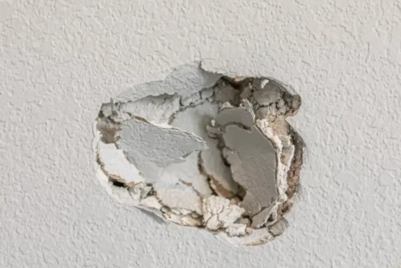 Hole punched in an interior drywall wall, awaiting patch and repair