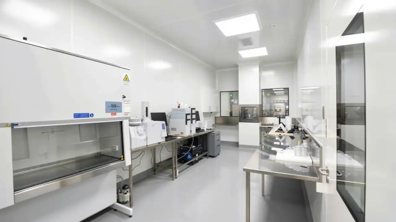 An equipped laboratory cleanroom with seamless sealed white wall panels, a fume hood and instrument benches