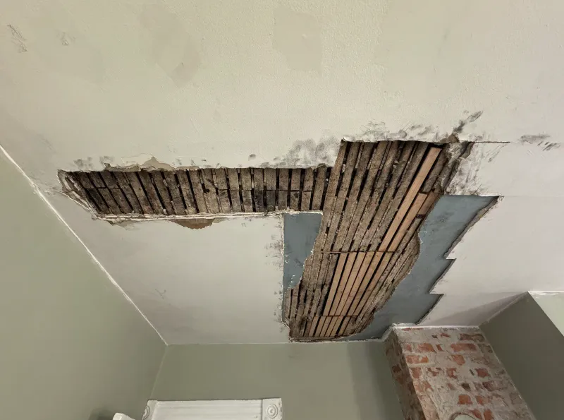 Ceiling plaster collapsed in two areas exposing wood lath, with an old brick chimney breast alongside