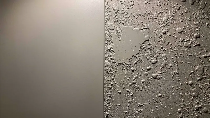 A smooth painted wall meeting a knockdown texture along a vertical line in raking light